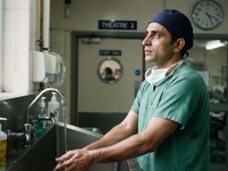 Surgeon wearing OT dress for surgeons, a green scrub suit, cap and mask, at a scrub sink outside an operating theatre in Pakistan
